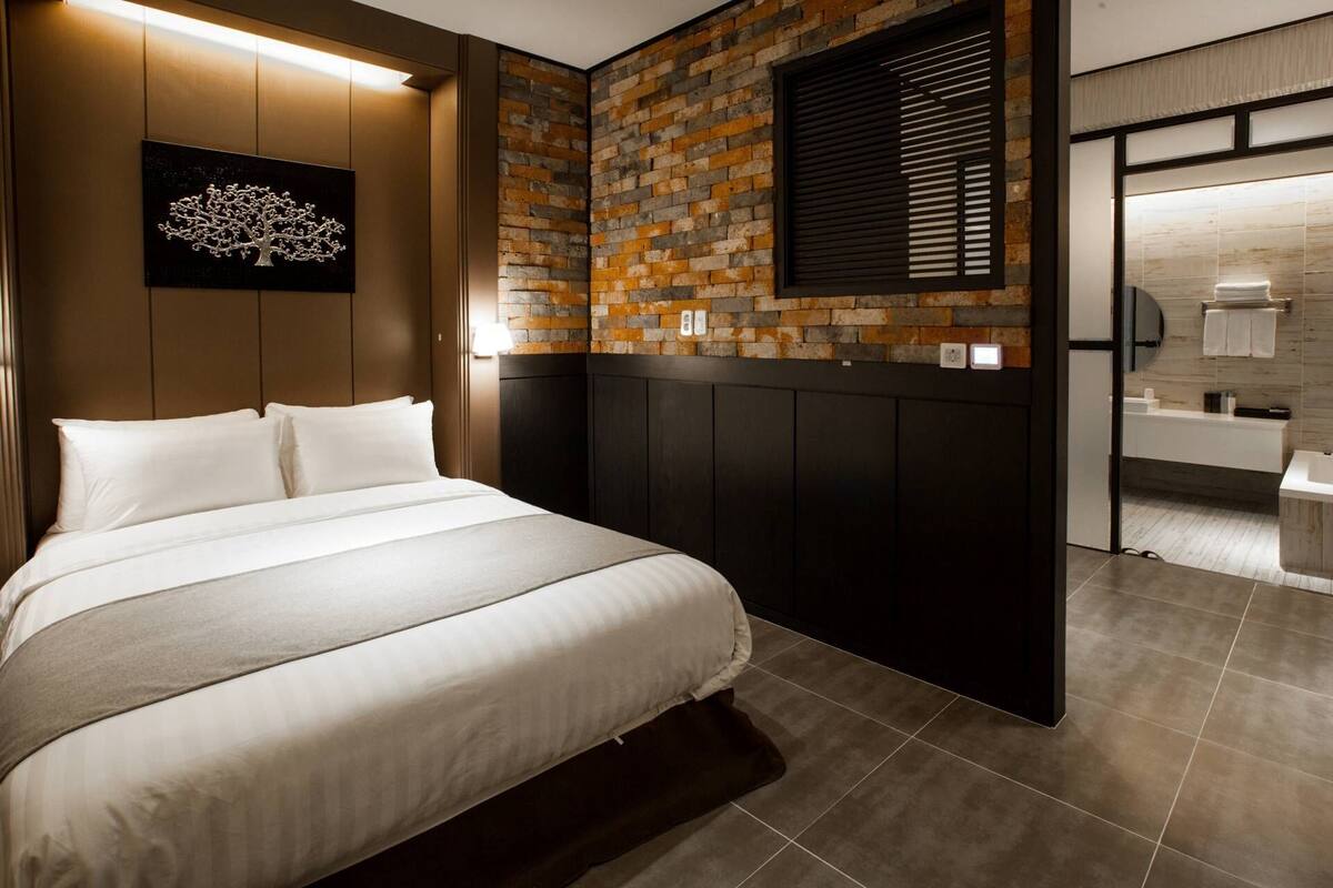 Ein modernes Hotelzimmer mit einem großen Bett, einer Ziegelwand, einem Wandbild und einem durchgegangenen Tür angedeuteten Badezimmer.