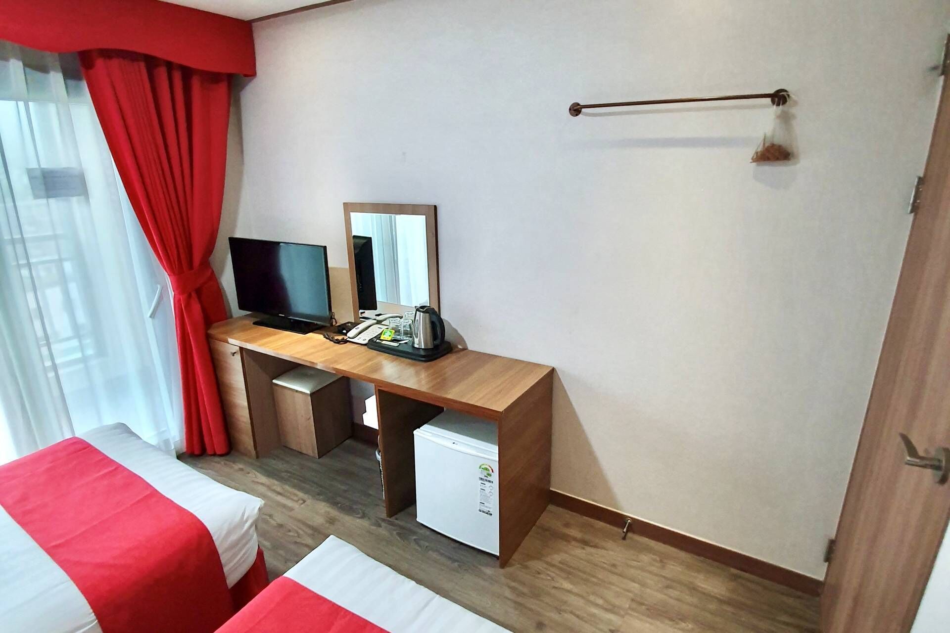 A hotel room with a wooden desk, a television, a mini-fridge, and a bed with red and white bedding.