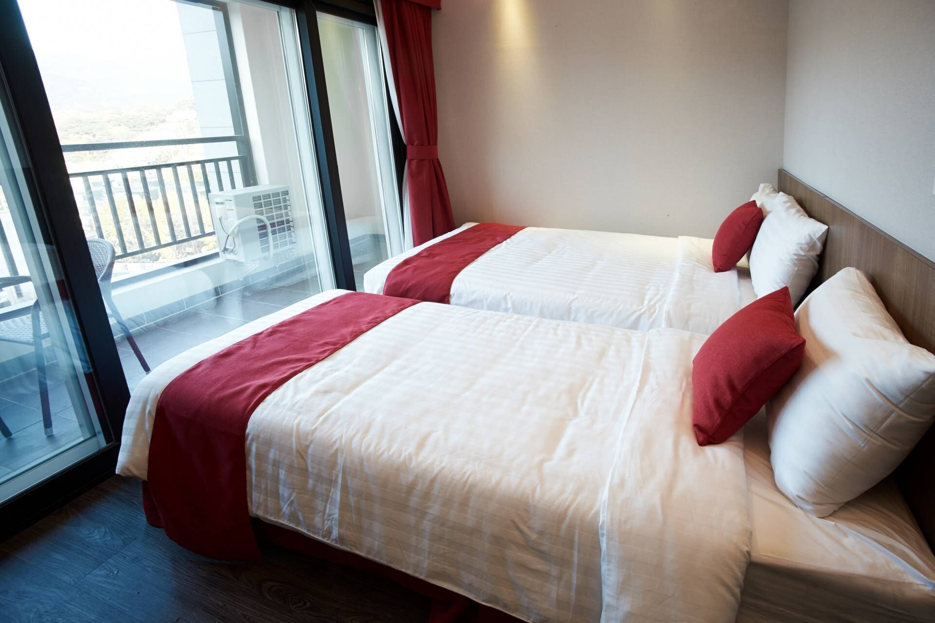 A hotel room with two beds, a balcony, and a view of the outdoors.
