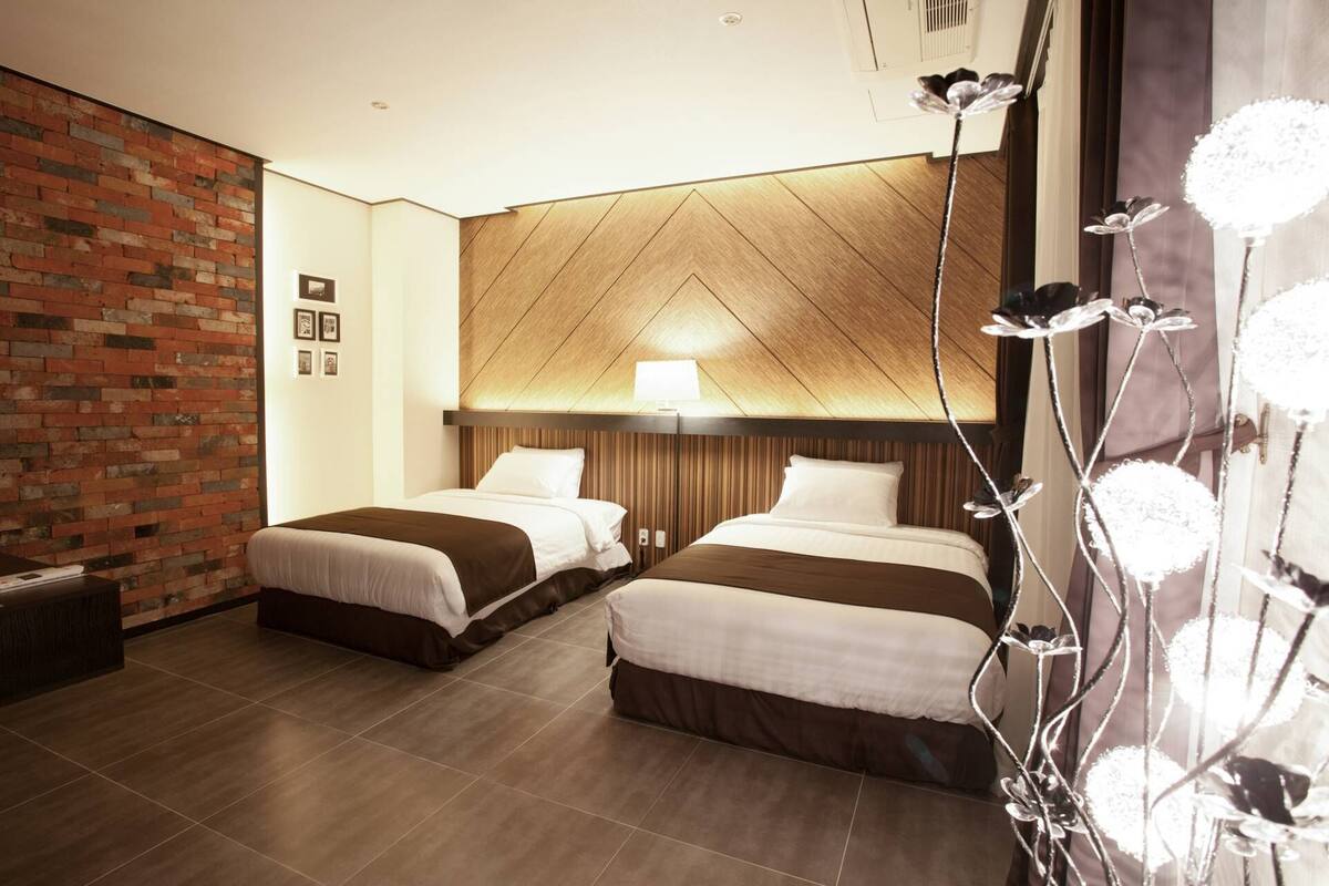 Ein Hotelzimmer mit zwei Betten, einer Ziegelwand, einer Holzbalkendecke und einer dekorativen Leuchte.