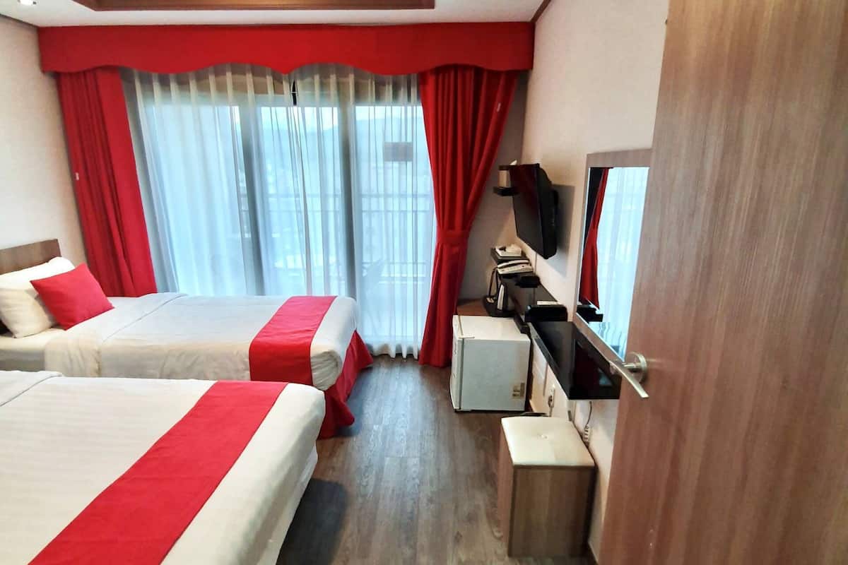 Ein Hotelzimmer mit zwei Betten, einem Schreibtisch, einem Fernseher und einem Fenster mit Vorhängen.