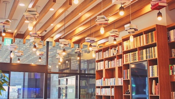 Ein Bibliotheksraum mit Bücherregalen, Pendelleuchten und einem Fernseher.