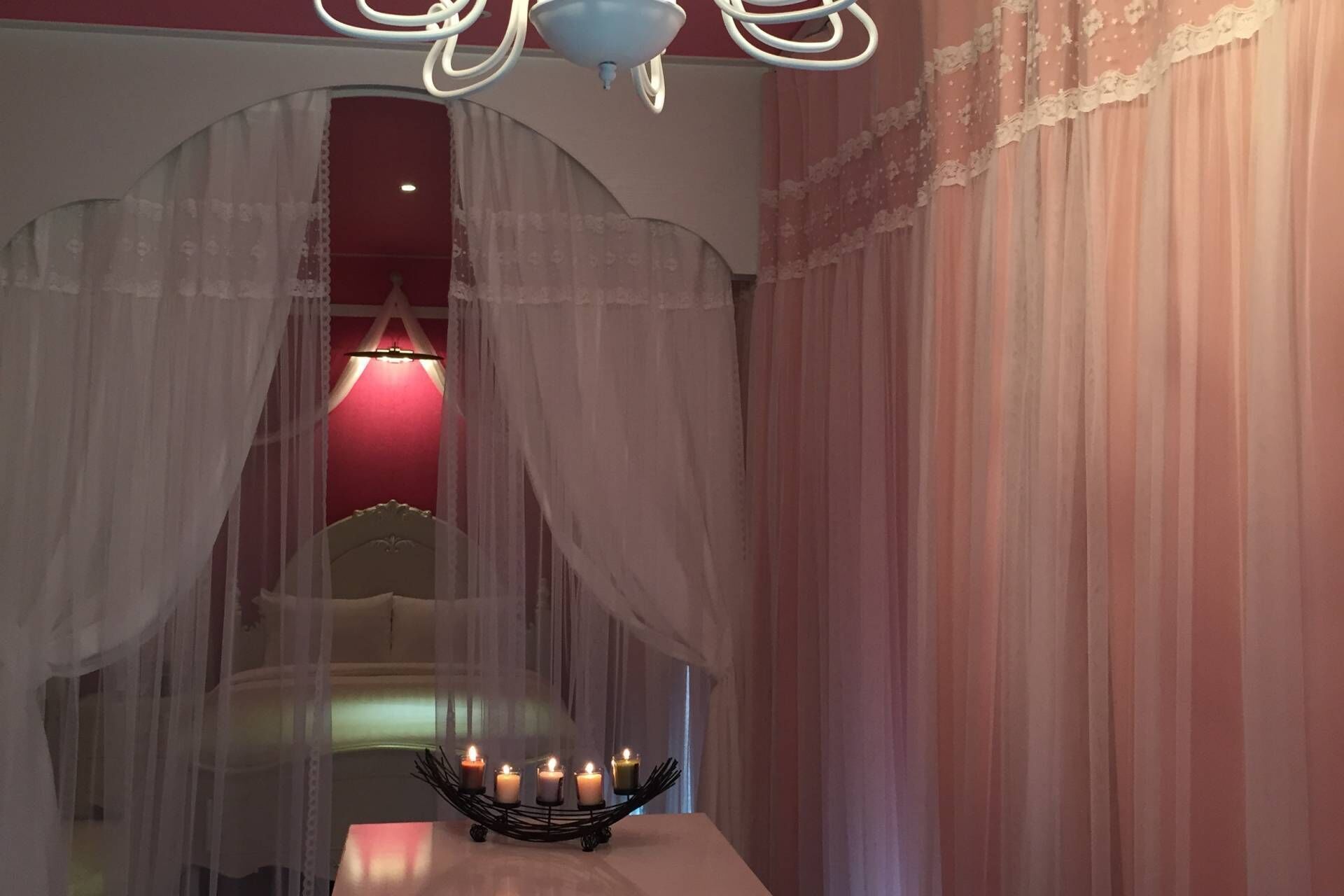 A room with a bed, a chandelier, and a table with candles.