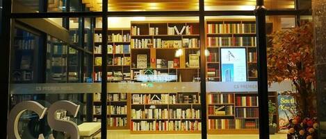 La entrada de un hotel con un llamativo letrero que dice 'CS PREMIER HOTEL', un interior bien iluminado con estanterías y una escalera que conduce a los pisos superiores.