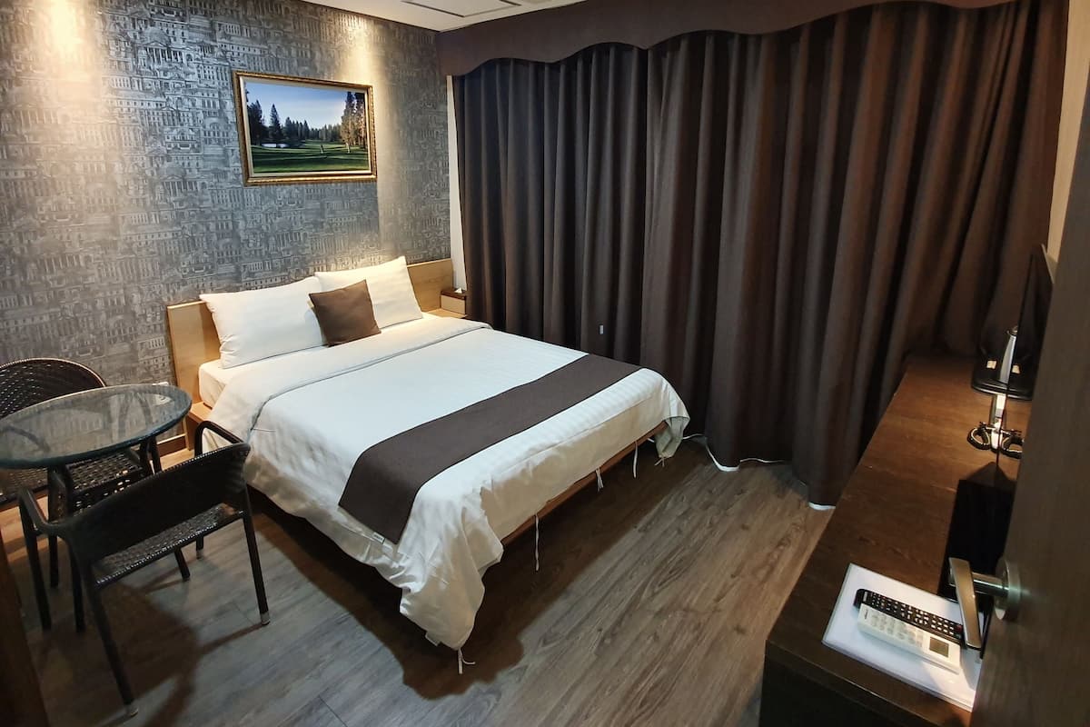 Ein Hotelzimmer mit Bett, Schreibtisch, Stuhl, einem Bild an der Wand und einem Vorhang.