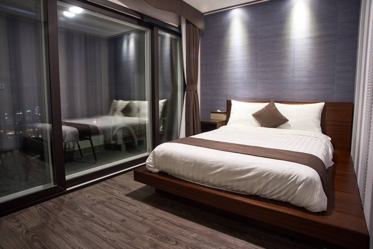 Ein modernes Hotelzimmer mit einem großen Bett, einer Glastür, die auf einen Balkon führt, und Blick auf die Stadt.