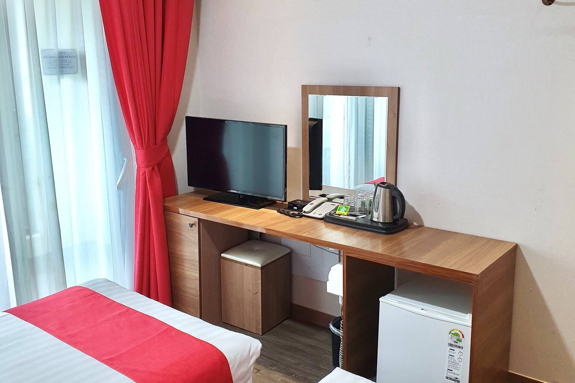 Quarto de hotel com cama, escrivaninha, televisão, espelho, máquina de café e mini-geladeira.