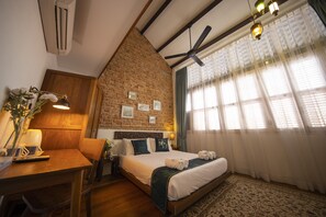 A bedroom with a brick wall, a wooden headboard, a bed with white linens, a desk with a lamp, and a window with sheer curtains. - Sweet Cili (George Town)