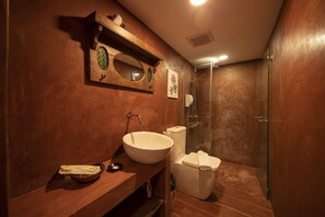 A bathroom with a wooden vanity, a large oval sink, a toilet, and a glass-enclosed shower. - Sweet Cili (George Town)