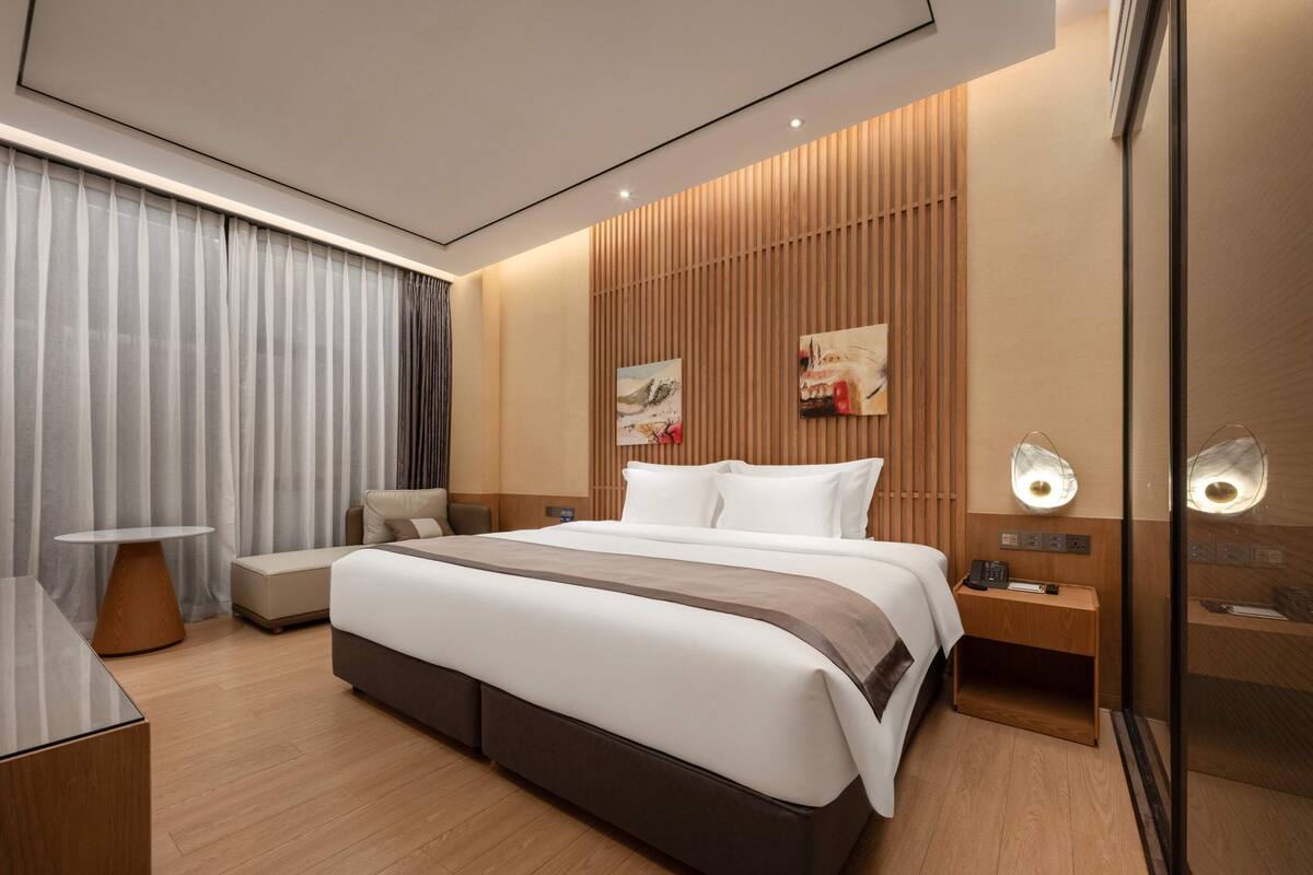 Una habitación de hotel moderna con una cama grande, una mesita de noche, una silla, un escritorio y un espejo.