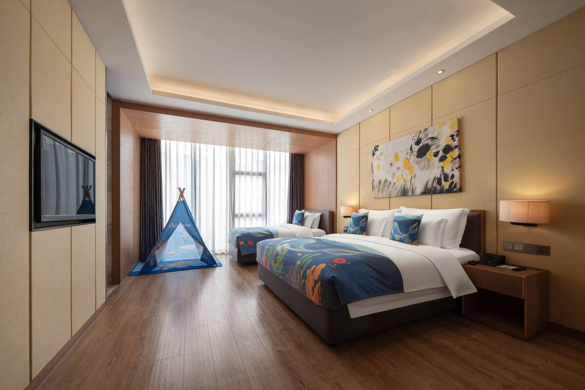 Habitación de hotel con una cama grande, un escritorio, una silla, un ventanal y un televisor montado en la pared.
