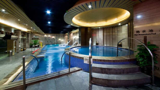 A high-temperature pool area with a large, curved ceiling light fixture, a small hot tub, and a sign indicating the pool's name. - Palm Spring Hotel (Zhuhai)