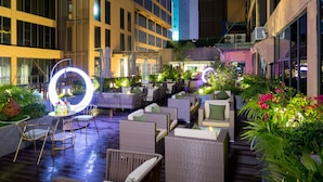 An outdoor seating area with wicker furniture, a neon sign, and lush greenery. - Palm Spring Hotel (Zhuhai)