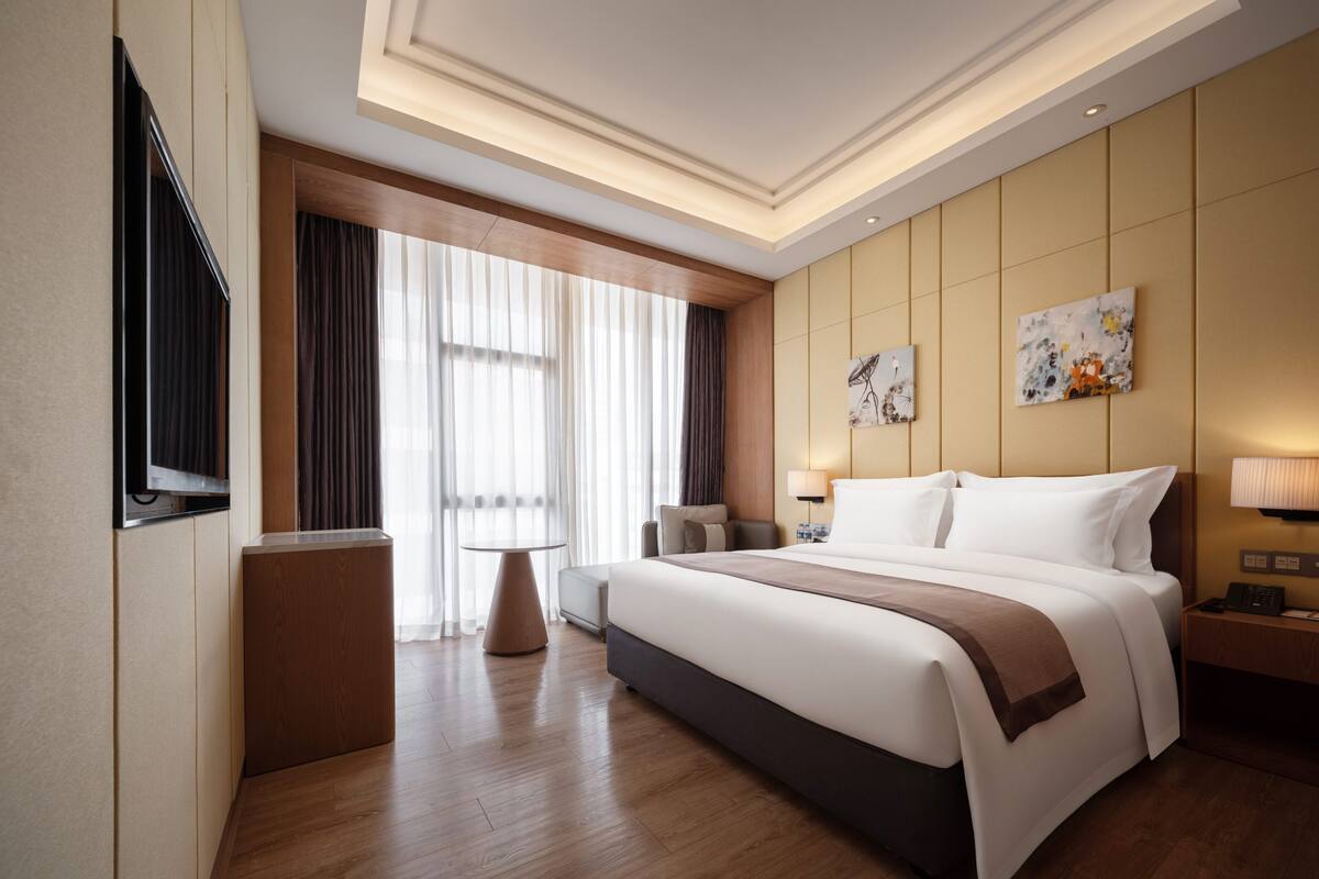 Habitación de hotel con una cama grande, televisión, escritorio, silla y obras de arte en las paredes.