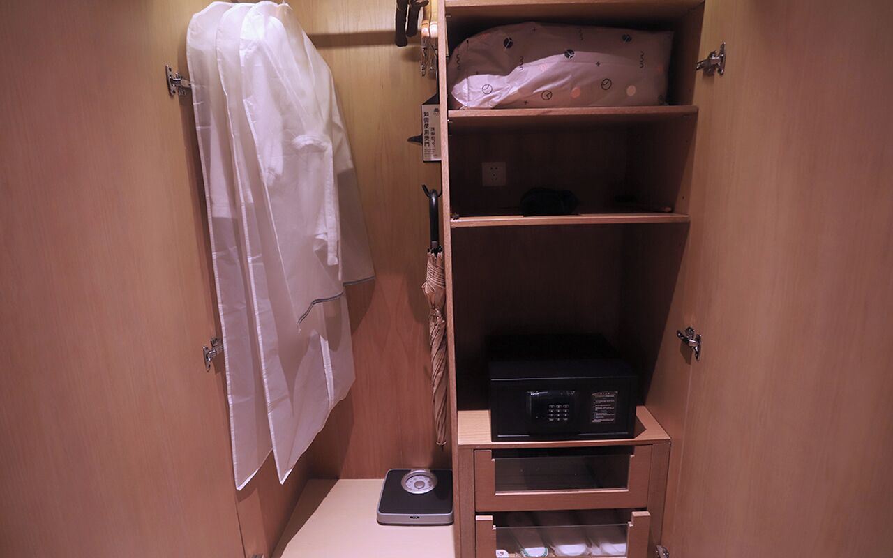 A small bathroom with a scale, a shelf with a pillow, and a towel hanging on a hook.