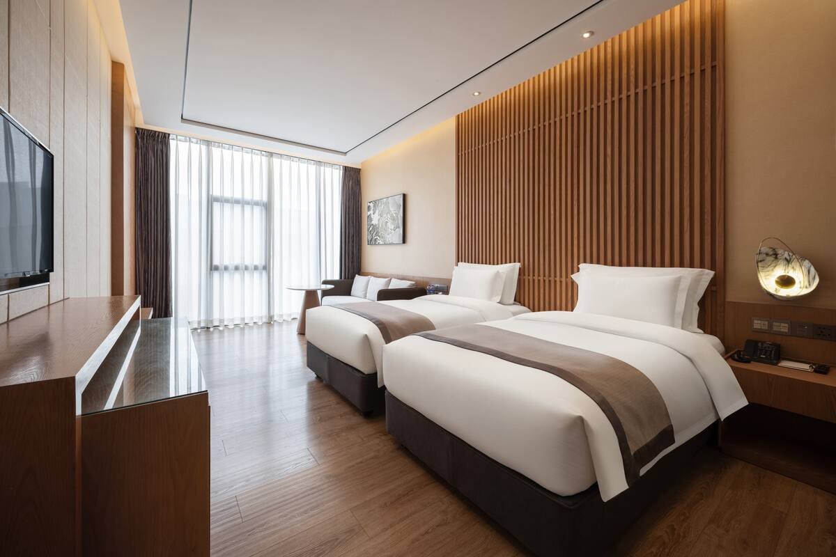 Una habitación de hotel moderna con una cama grande, televisor, escritorio y ventana con cortinas.