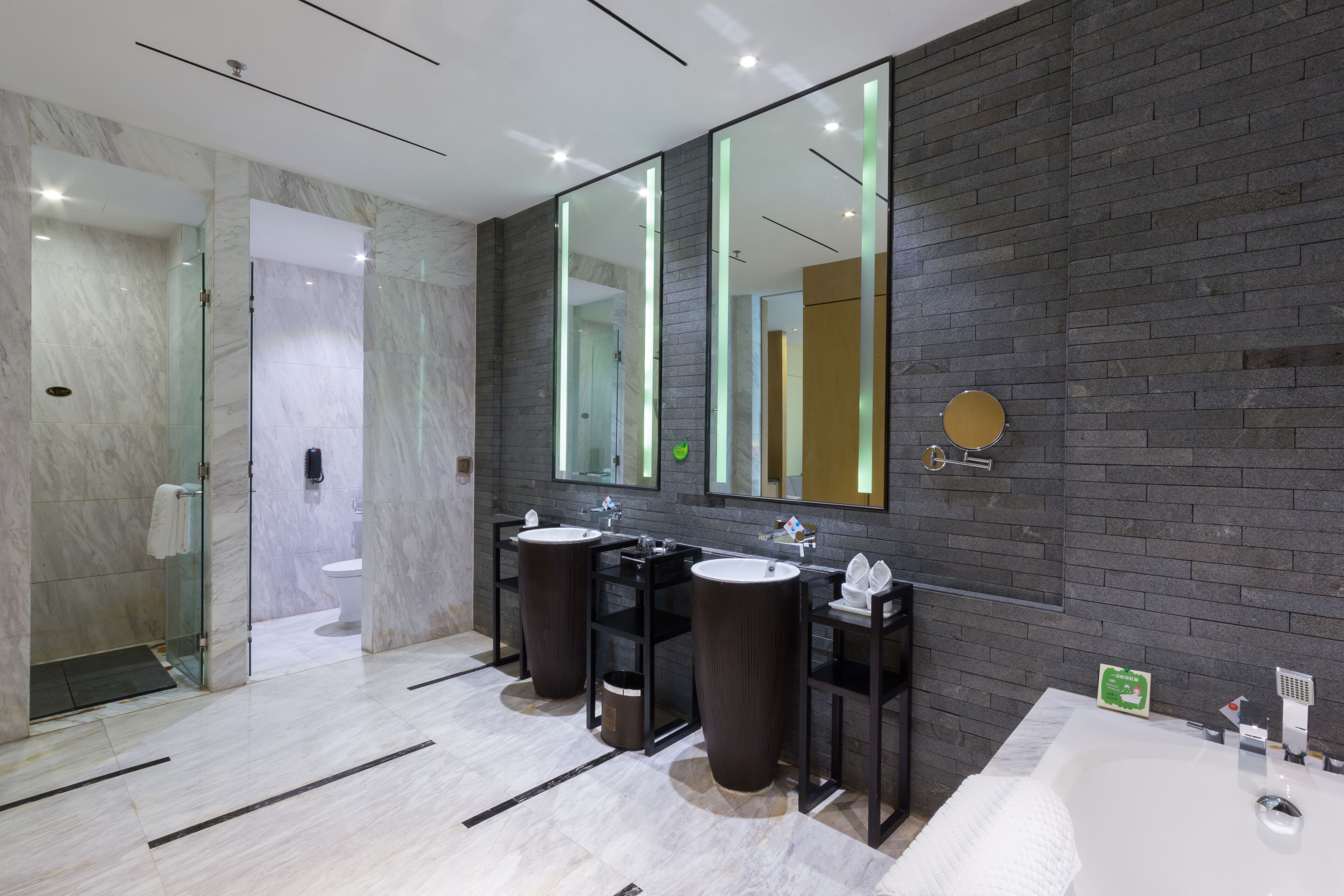 A modern bathroom with two sinks, a large mirror, and a bathtub.