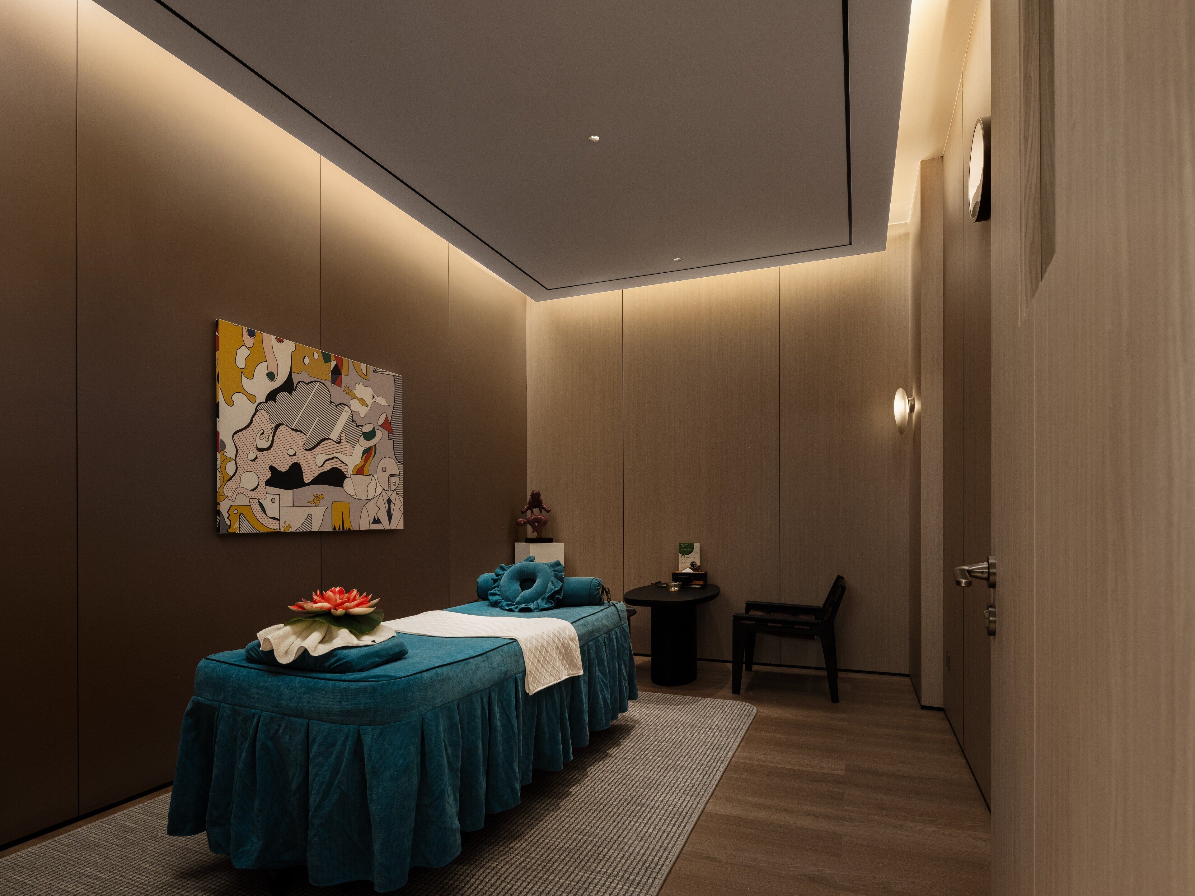A modern spa room with a massage table, a small massage chair, and a wall-mounted massage table.