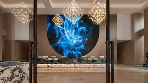 A modern lobby with a large digital screen displaying a blue abstract image, a marble reception desk, and contemporary lighting fixtures. - Palm Spring Hotel (Zhuhai)