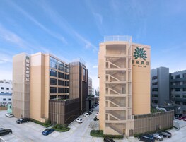 Un hotel moderno con un llamativo letrero vertical, una escalera central y un estacionamiento.