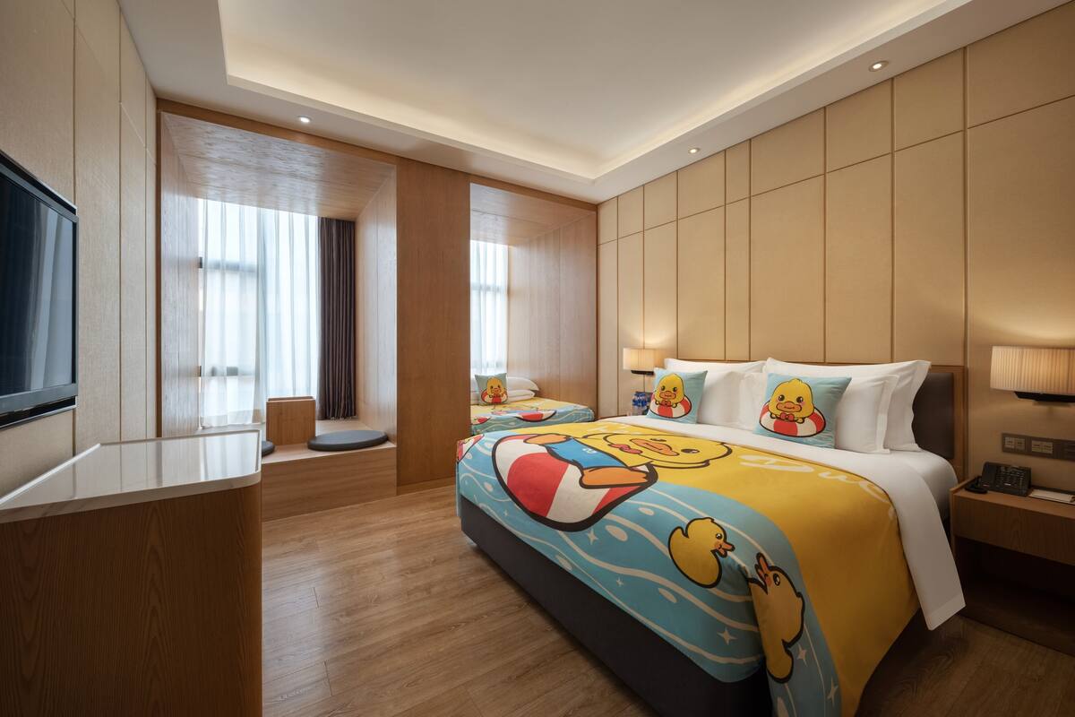 Una habitación de hotel con una cama grande, televisión, zona de estar y ventana con cortinas.