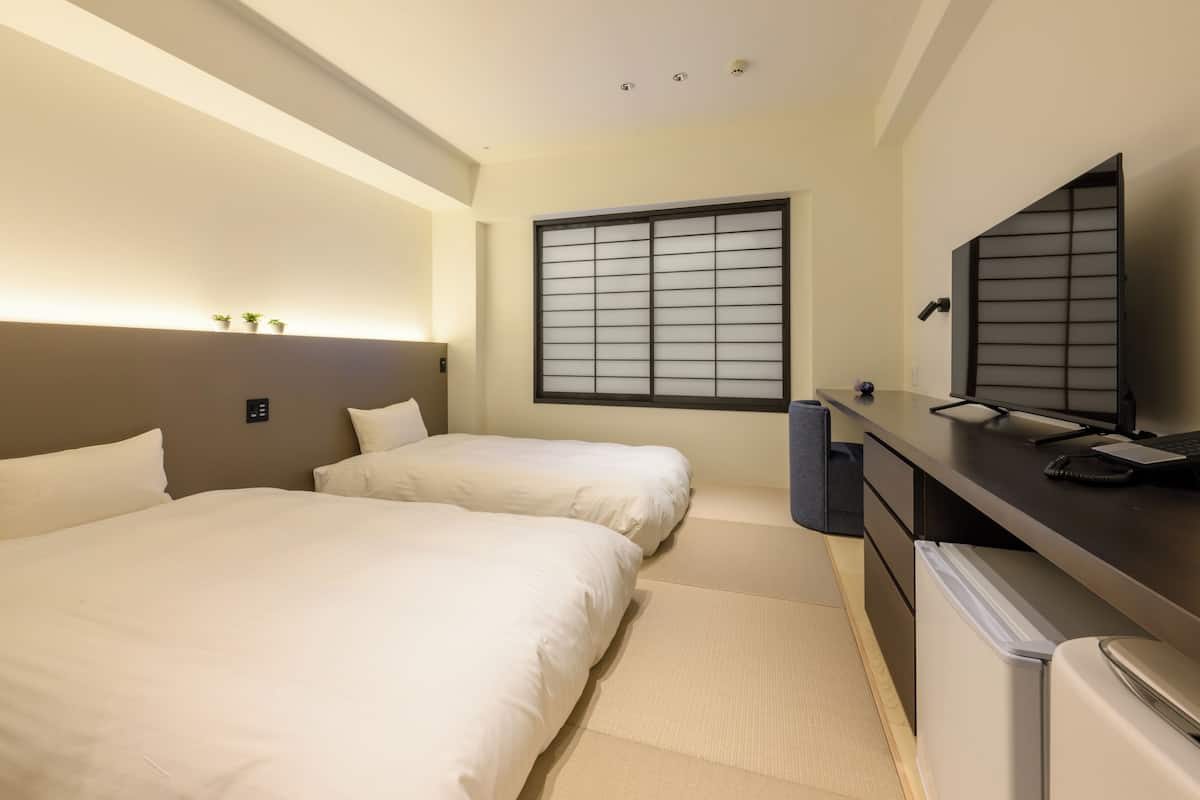 Ett hotellrum med två sängar, ett skrivbord med en dator, en TV och ett fönster med utsikt.