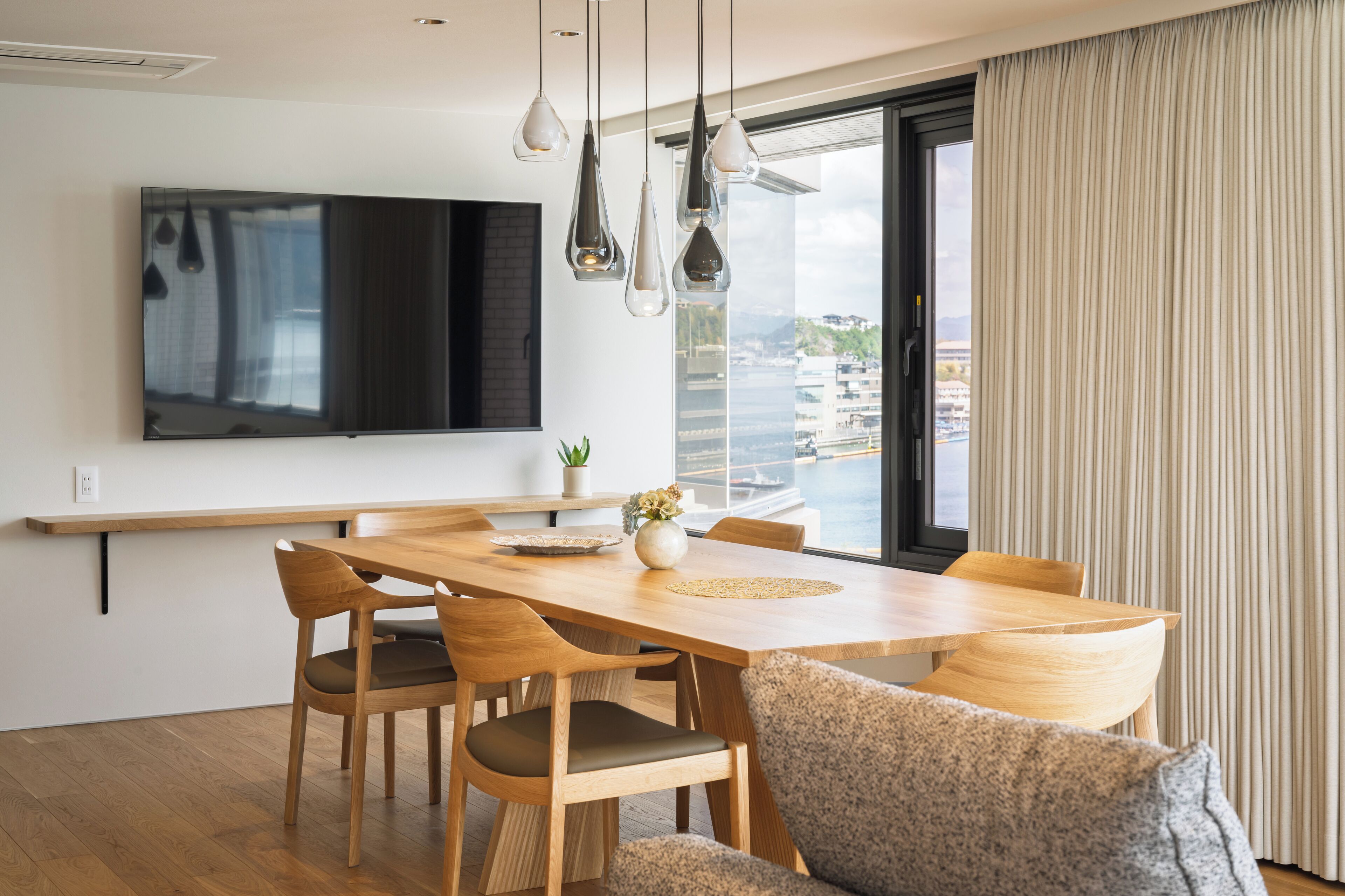 A modern dining area with a wooden table, chairs, and a flat-screen TV mounted on the wall.