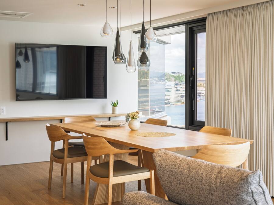 A modern dining area with a wooden table, chairs, and a flat-screen TV mounted on the wall.