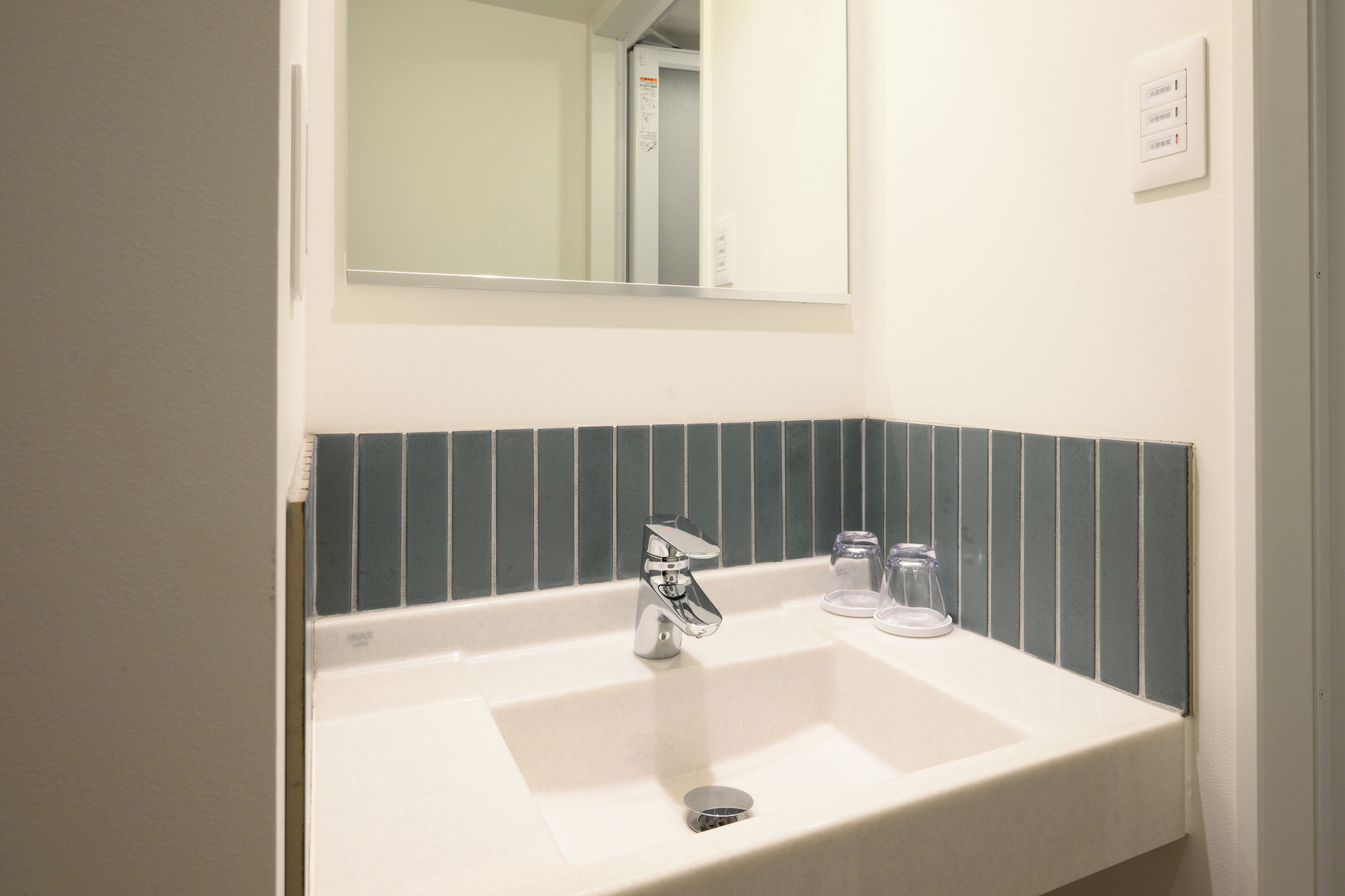 A bathroom with a white sink, chrome faucet, and a mirror above it. There are two clear glass bottles on the sink.