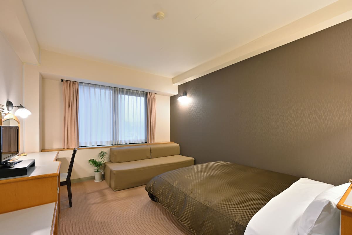 Ett hotellrum med en säng, ett skrivbord, en stol, en soffa och ett fönster med gardiner.