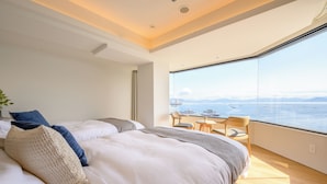 A modern hotel room with a large bed, a small table, and a view of the sea.