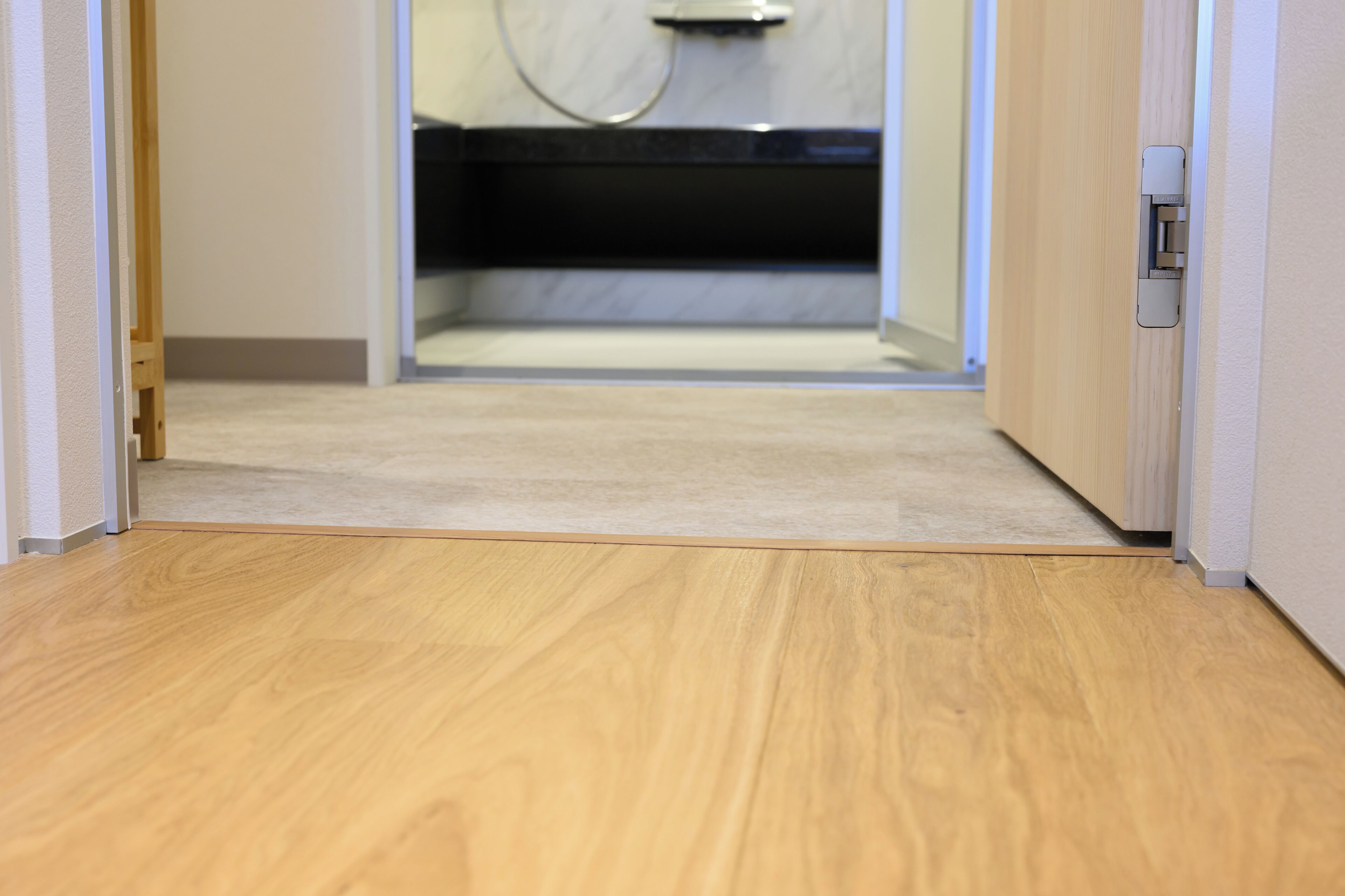 A wooden floor leading to a bathroom with a black bathtub and a white wall.