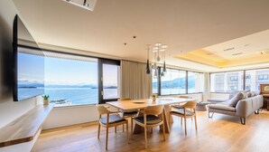 A modern living room with a large dining table, comfortable seating, a sofa, and a TV mounted on the wall.