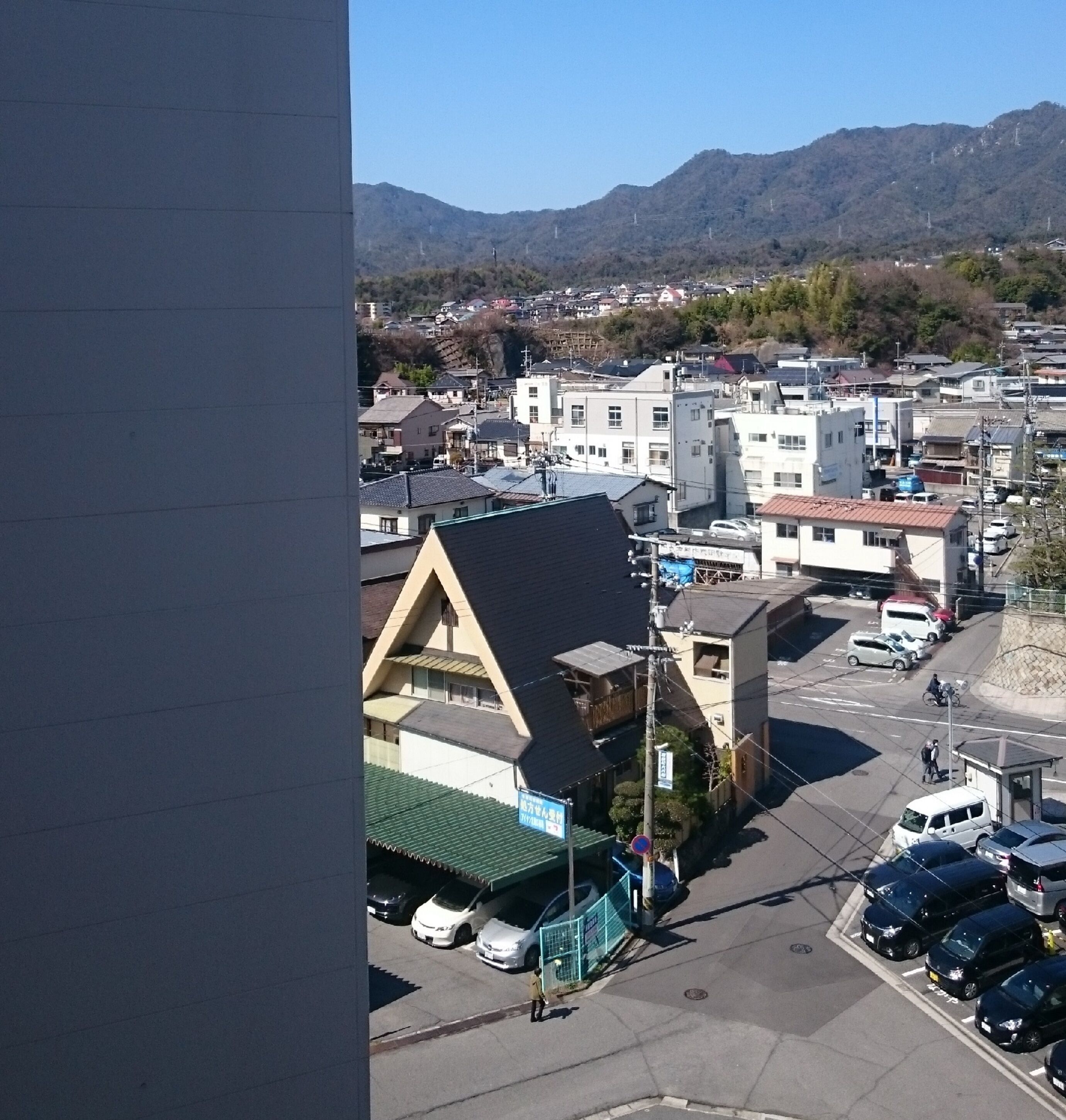 Zona residencial con edificios, coches estacionados y una montaña al fondo.