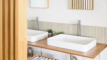 Un baño moderno con dos lavamanos blancos, encimeras de madera y una pequeña planta en maceta.