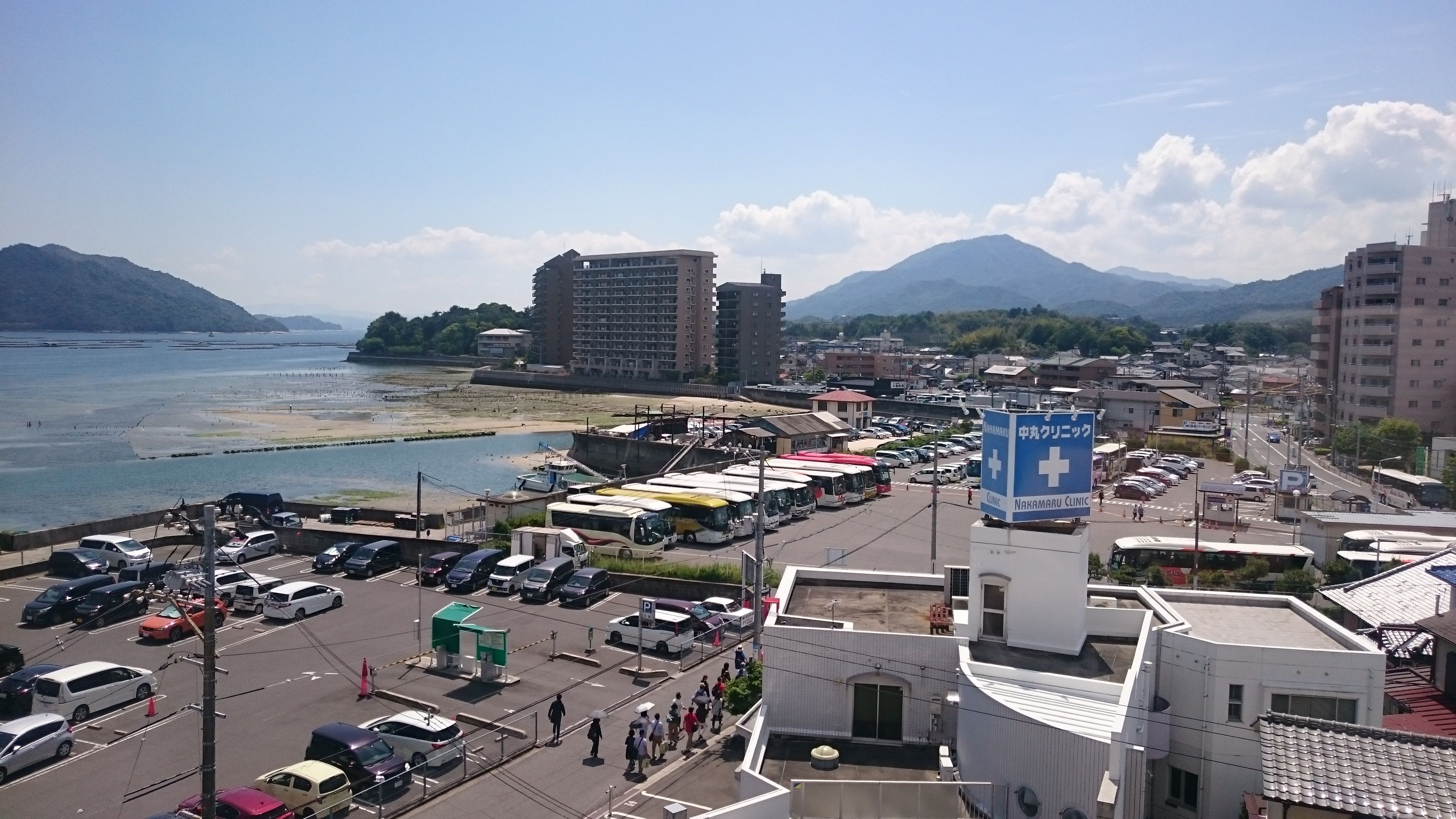 Un paysage urbain le long de la côte, avec un parking, des autobus et une enseigne indiquant la présence d’une clinique.
