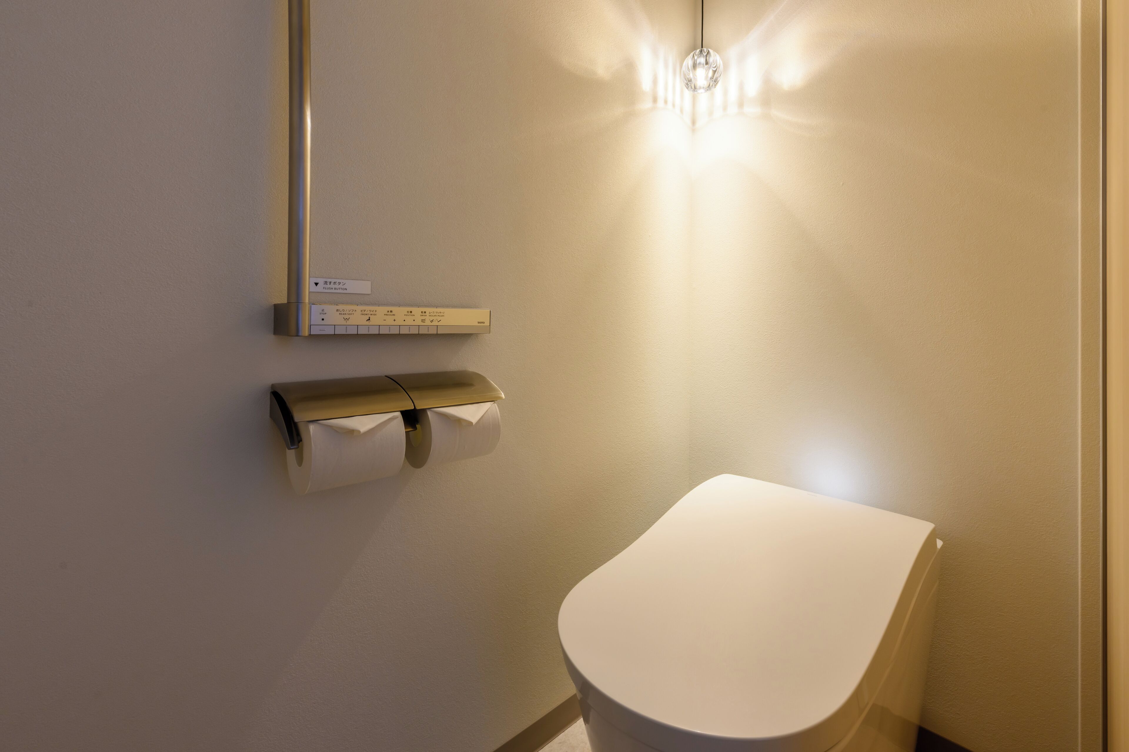 A modern bathroom with a toilet, a paper towel dispenser, and a wall-mounted thermostat.