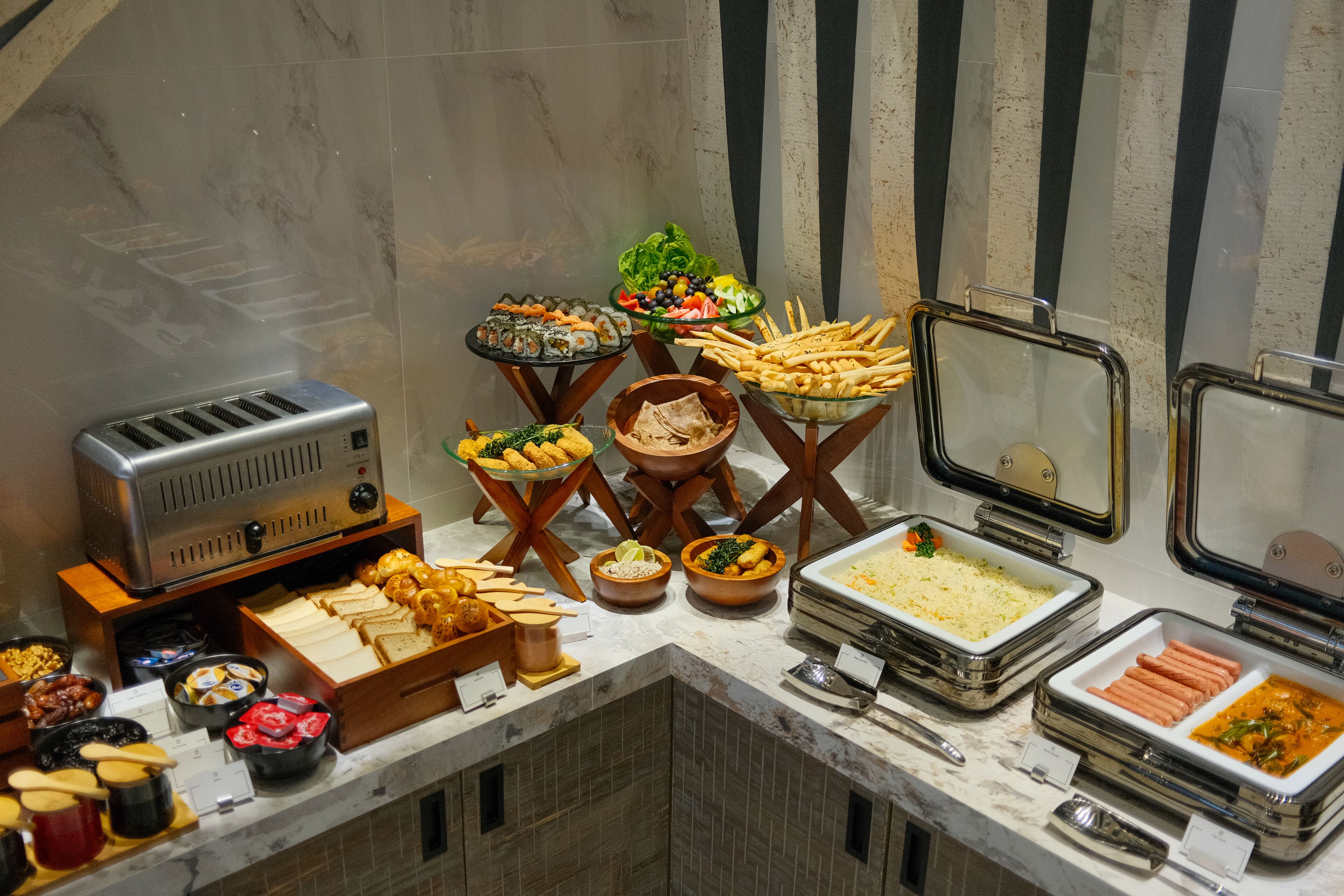 A buffet with various food items including bread, fruits, and hot dogs.