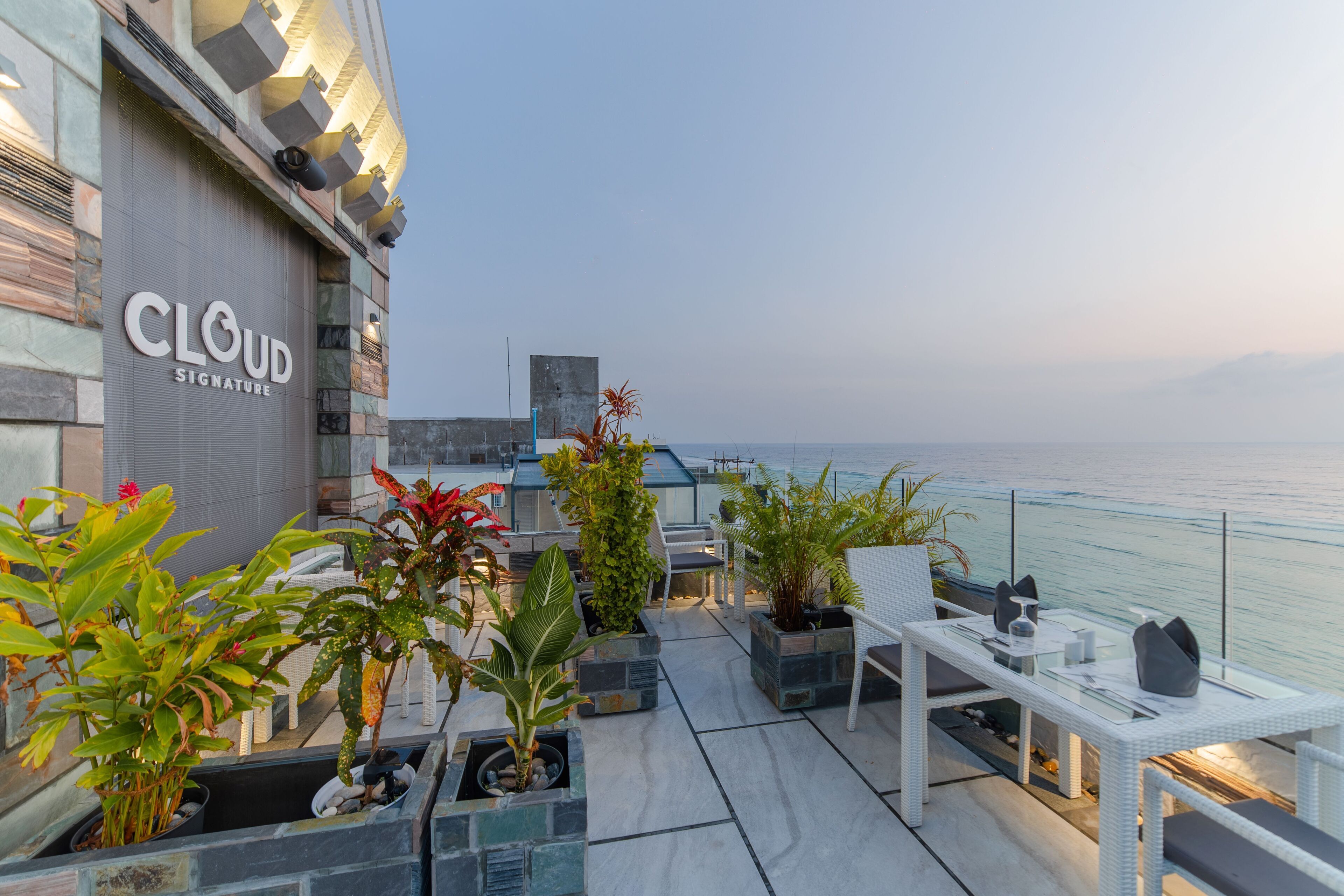 A rooftop terrace with outdoor seating, potted plants, and a view of the sea.