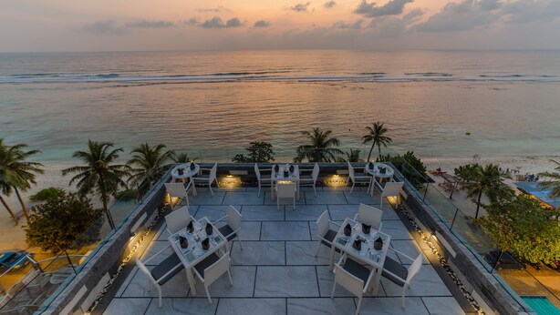 Eine Dachterrasse mit Sitzgelegenheiten im Freien und Blick auf das Meer bei Sonnenuntergang.