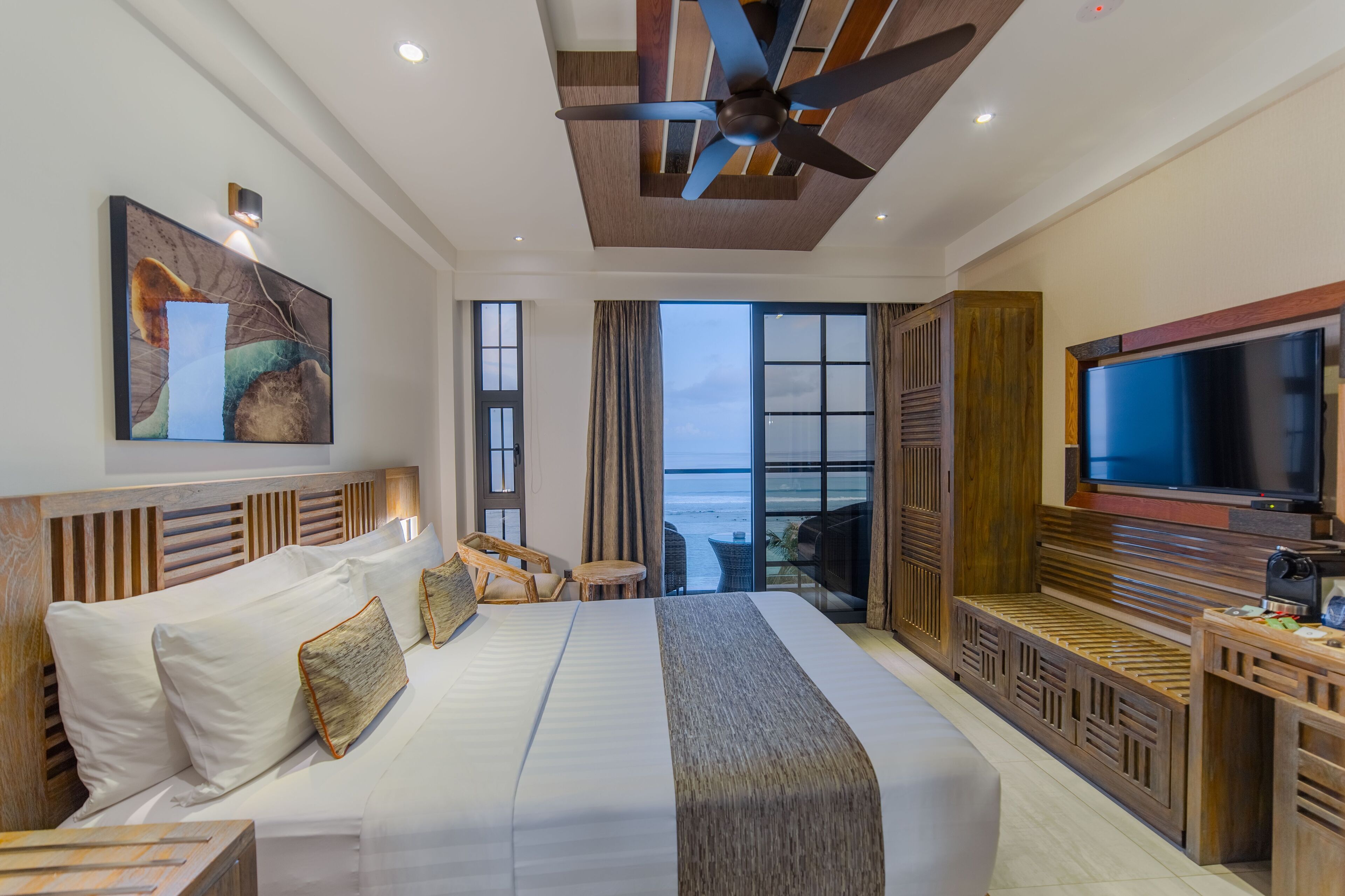 Habitación de hotel con una cama grande, televisor, ventilador de techo y vista al océano.