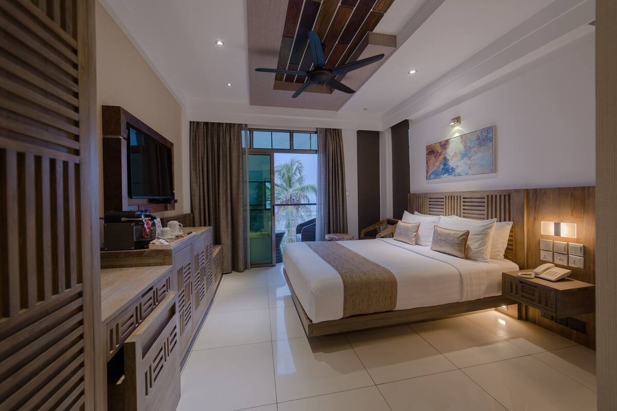 Habitación de hotel con una cama grande, ventilador de techo, televisor, escritorio con teléfono y ventana con cortinas.