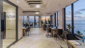Ein modernes Restaurant mit Meerblick, ausgestattet mit Marmorböden, zeitgenössischen Möbeln und einer Glaswand mit der Aufschrift "CLOUD Signature".