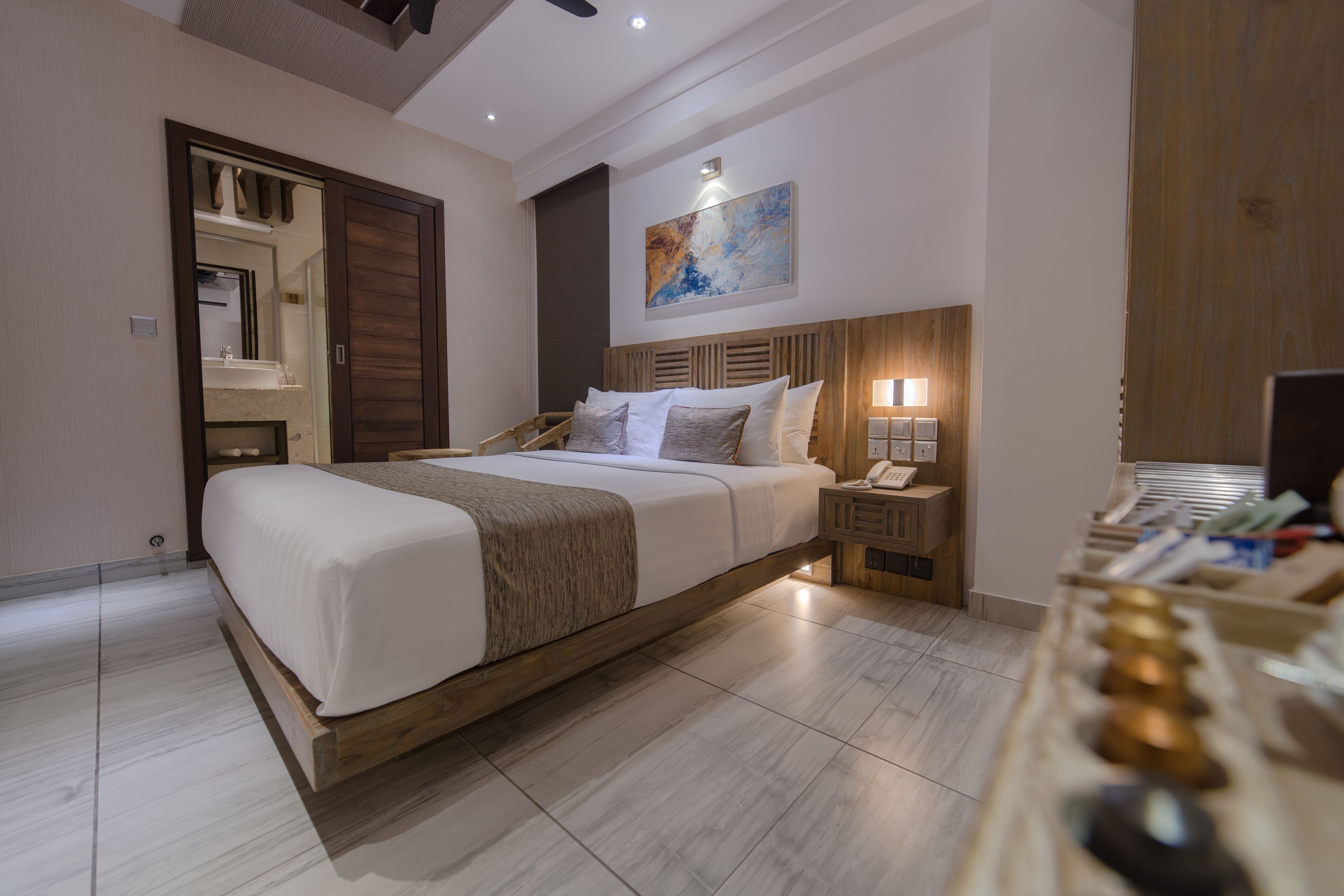 Una habitación de hotel moderna con una cama grande, cabecera de madera, mesitas de noche con lámparas y una pared de paneles de madera.