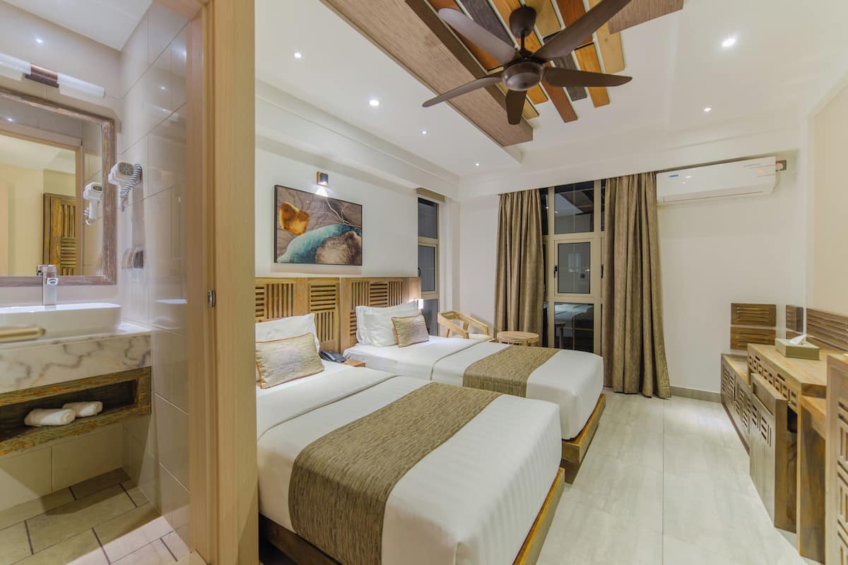 Habitación de hotel con dos camas, un baño con un espejo grande, un ventilador de techo y un equipo de aire acondicionado.