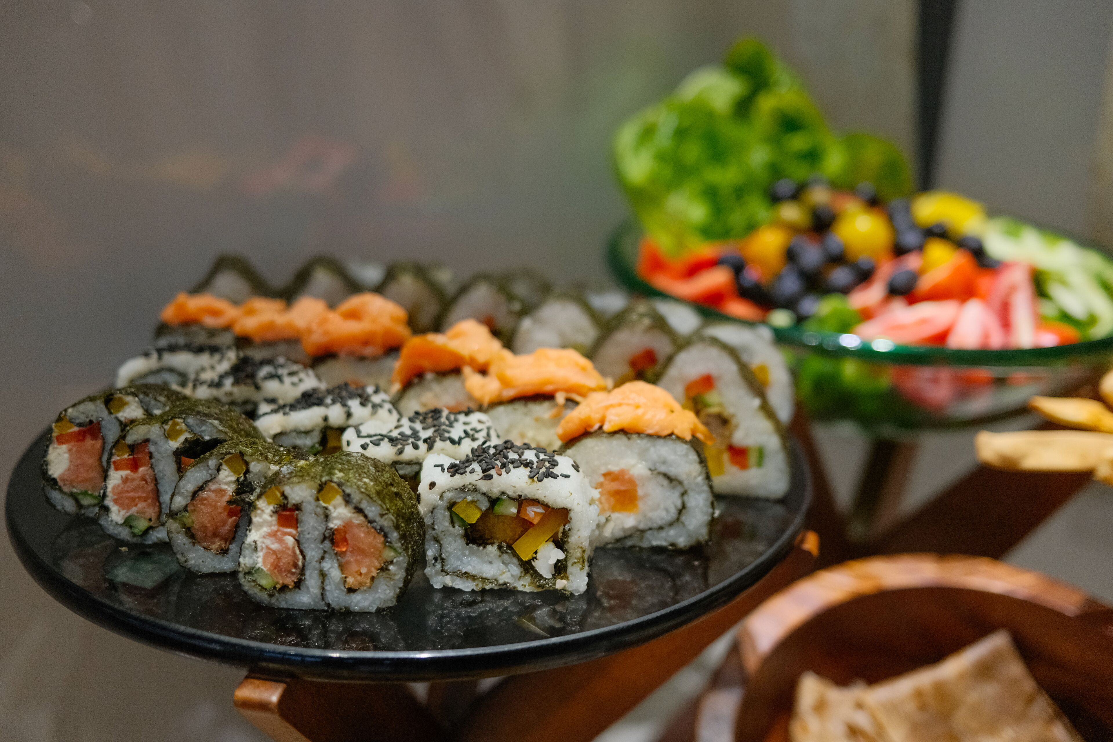 Une variété de rouleaux de sushi présentés sur un plateau noir, avec un saladier en arrière-plan.