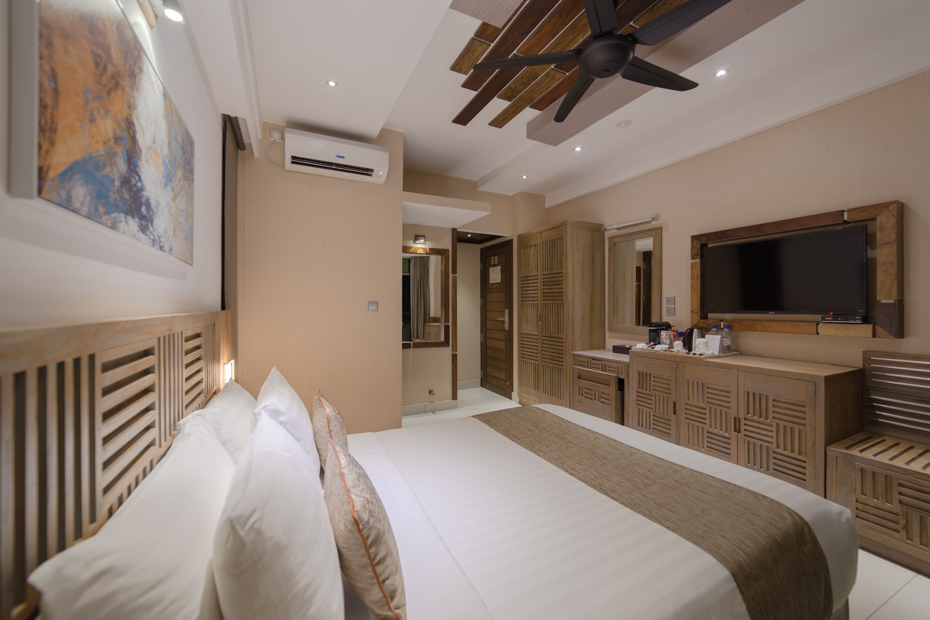 Habitación de hotel con cama, ventilador de techo, aire acondicionado, televisor y armario de madera.