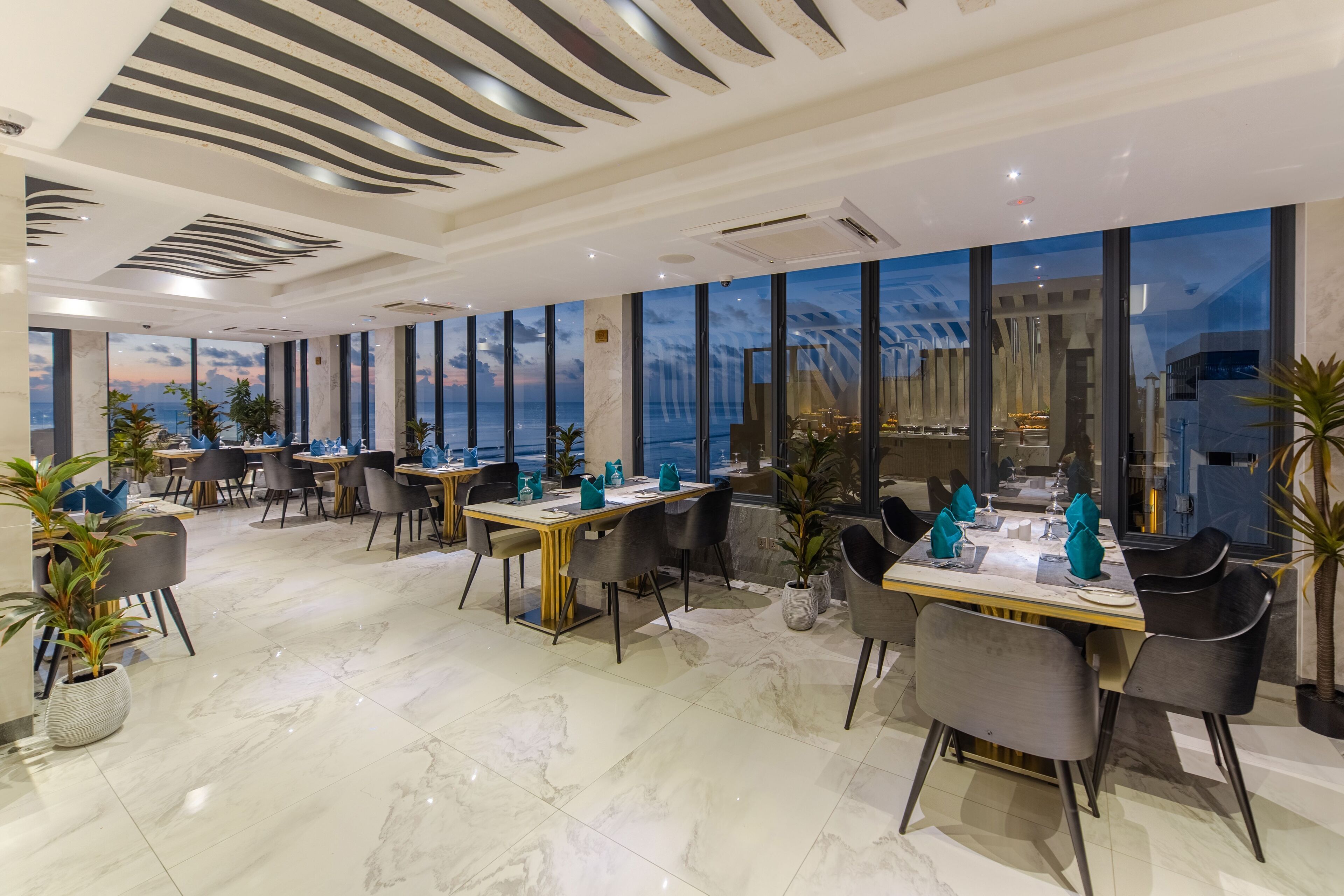 Un restaurante moderno con amplios ventanales, suelo de mármol y mobiliario contemporáneo.