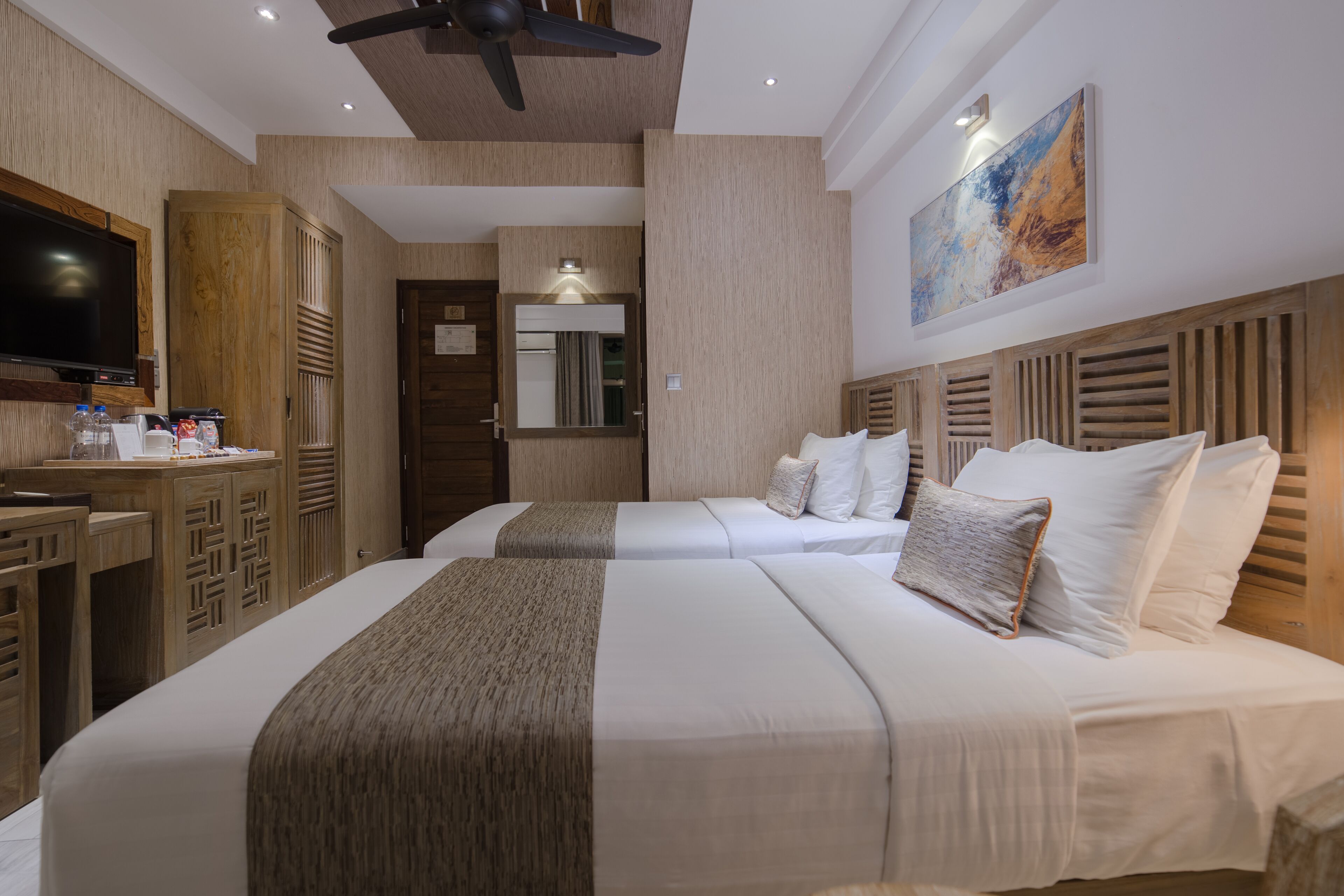 Ein Hotelzimmer mit zwei Betten, einem Fernseher, einem Schreibtisch und einem Spiegel.
