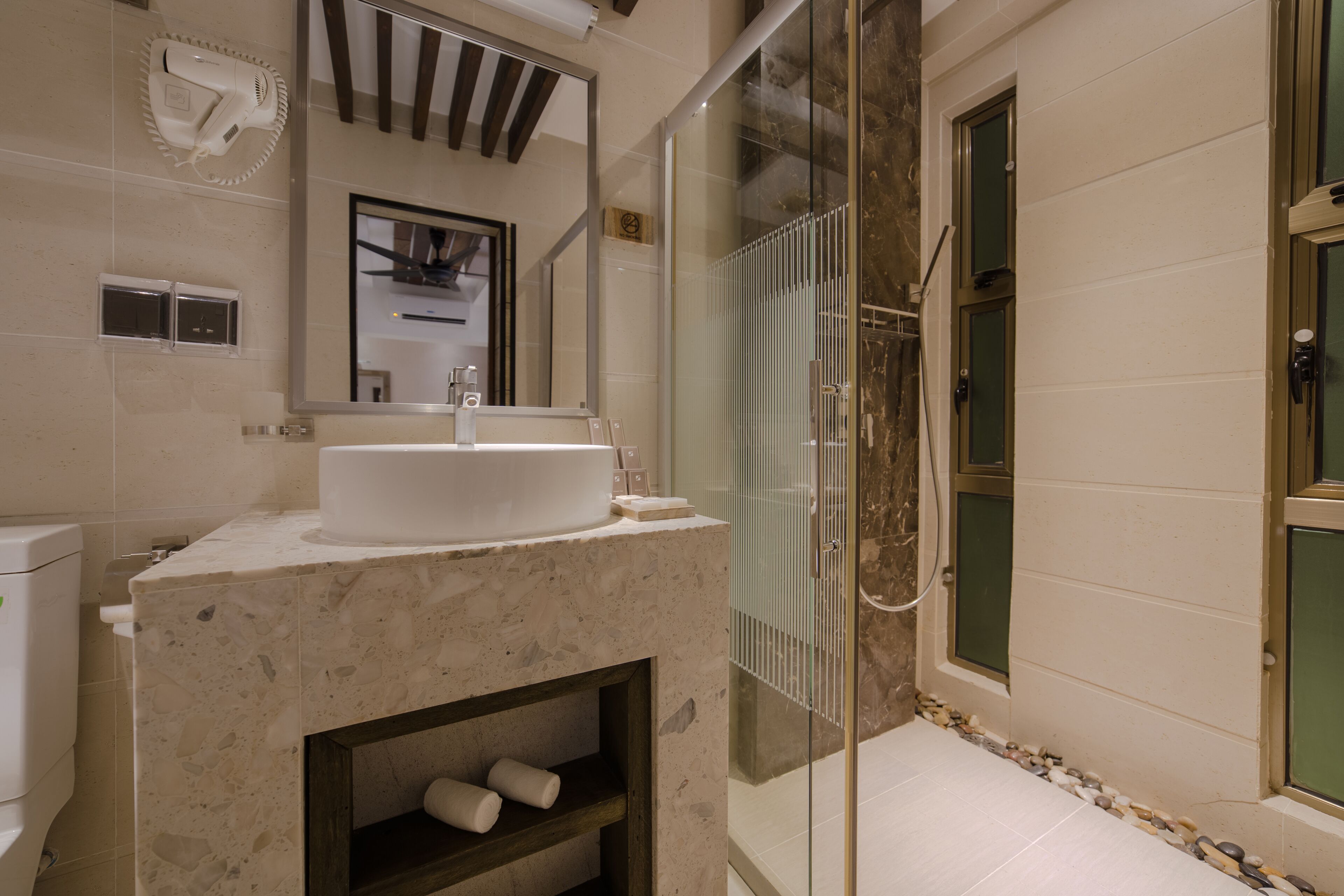 A bathroom with a marble sink, a glass shower enclosure, and a built-in shelf with toiletries.